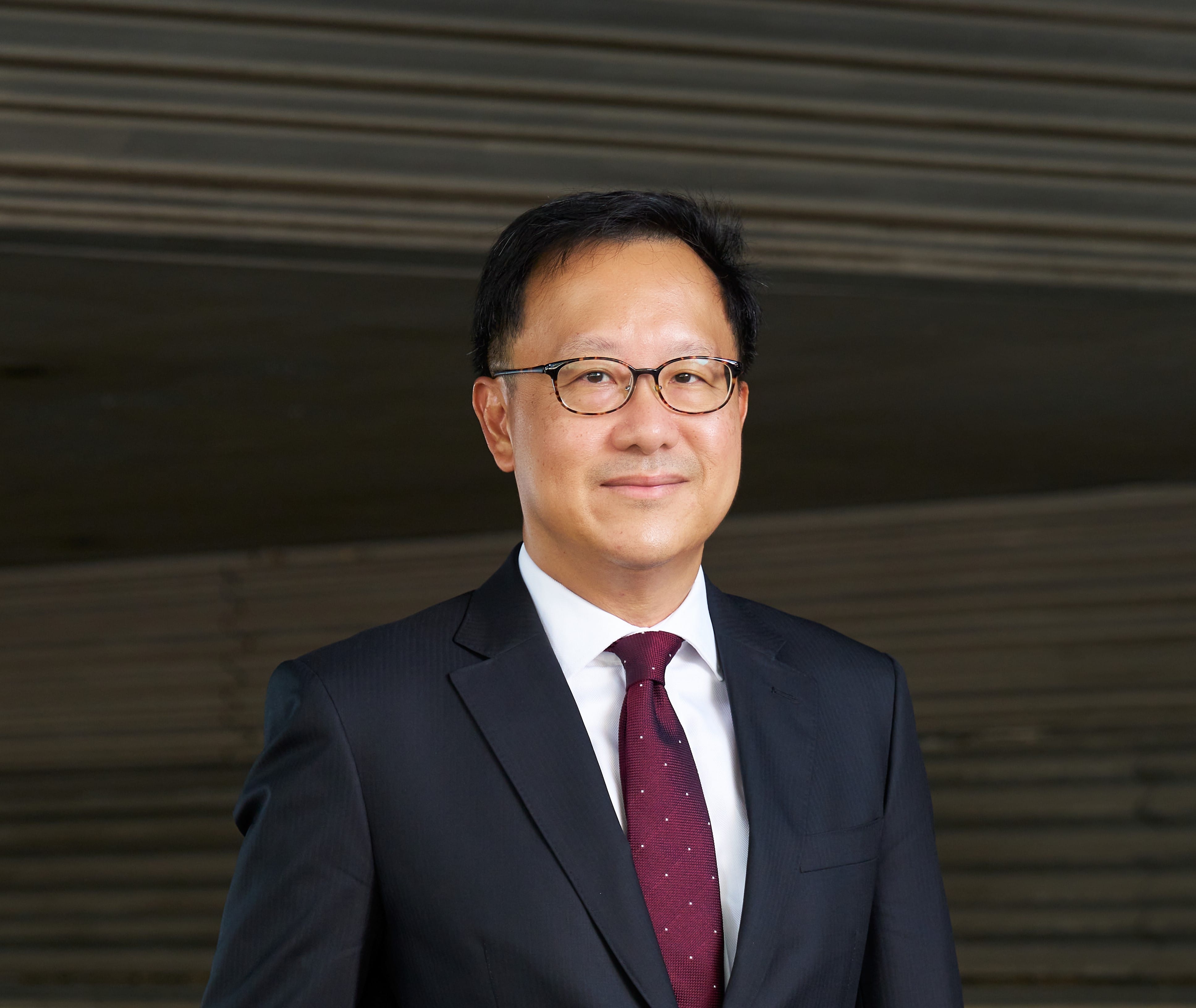 Portrait of a man wearing glasses, a dark suit, and a patterned red tie.